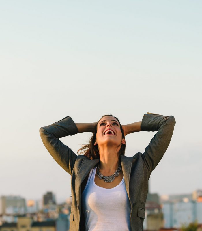 Successful young businesswoman after business or job achievement towards city background. Professional joyful woman outside.